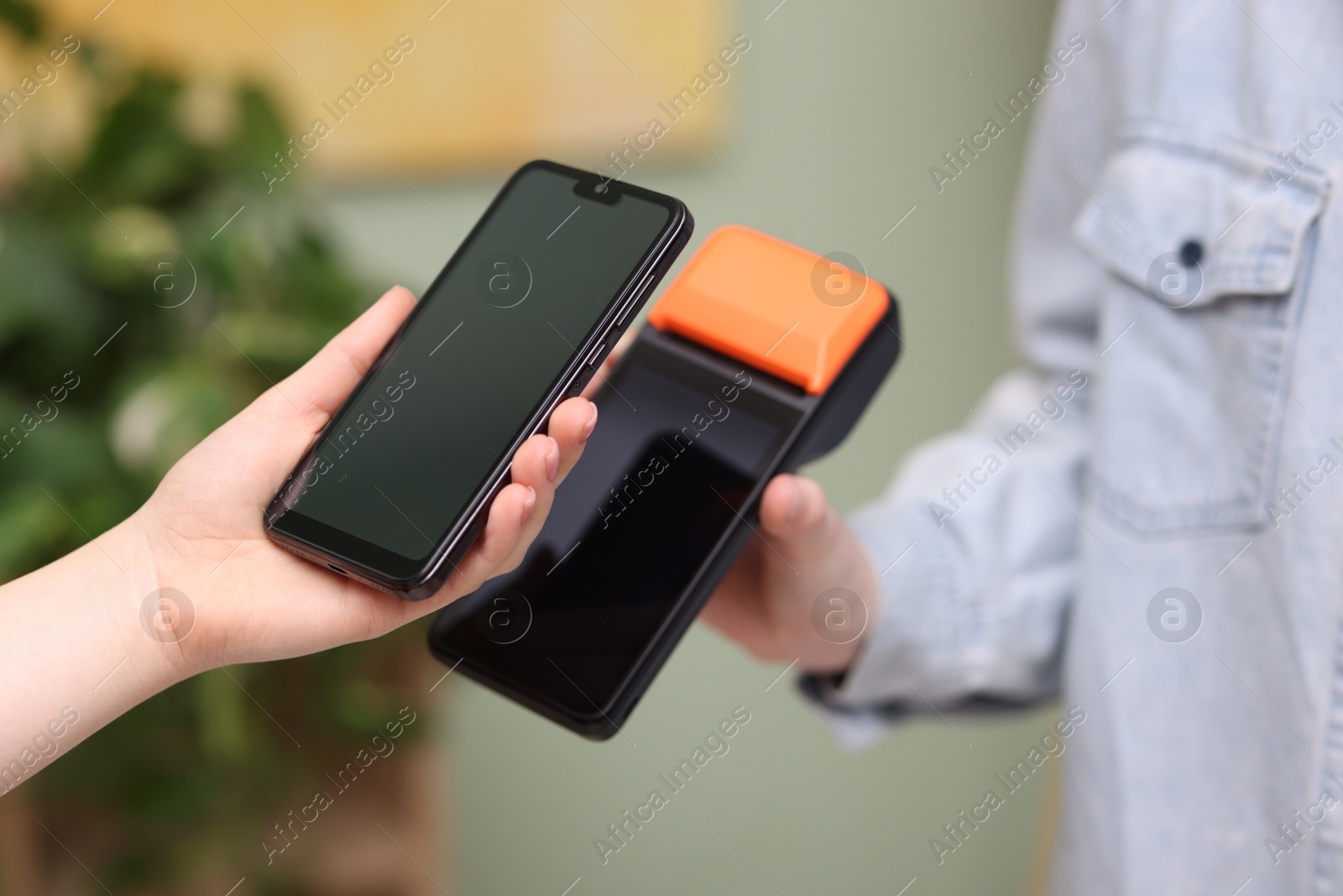 Photo of Woman paying with smartphone via terminal against blurred background, closeup