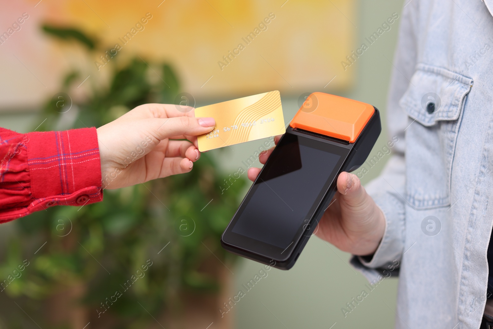 Photo of Woman paying with credit card via terminal against blurred background, closeup