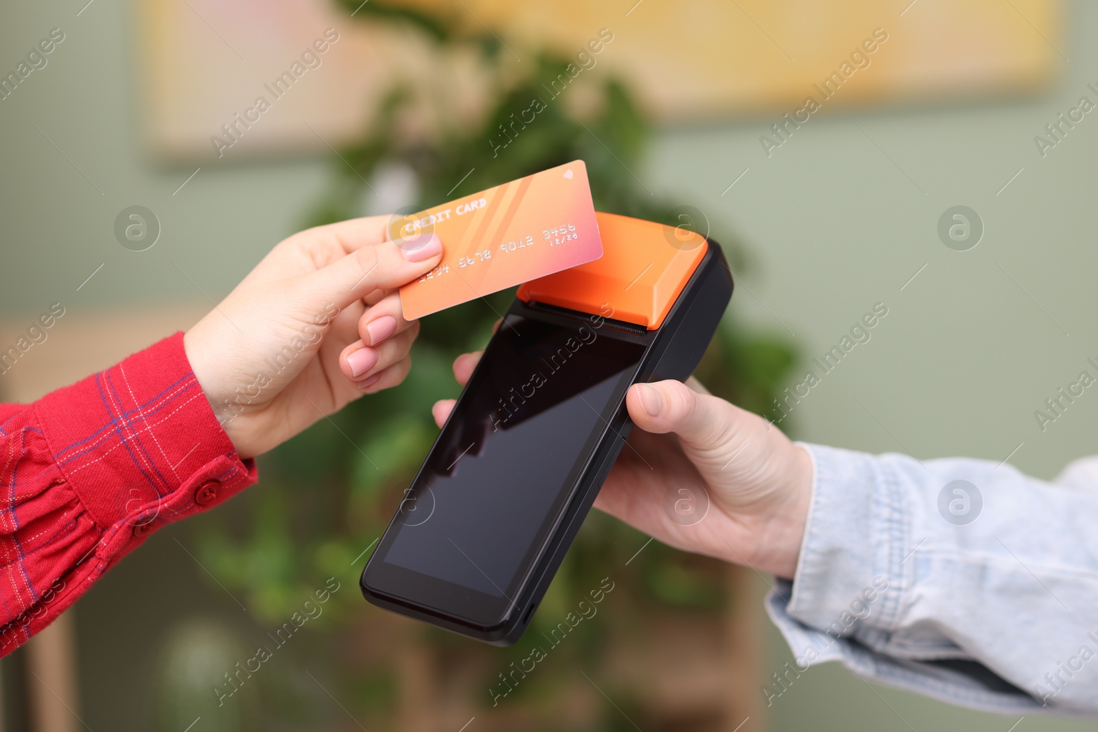 Photo of Woman paying with credit card via terminal against blurred background, closeup