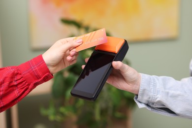 Photo of Woman paying with credit card via terminal against blurred background, closeup