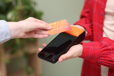 Photo of Woman paying with credit card via terminal against blurred background, closeup