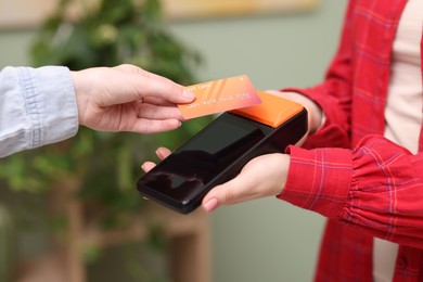 Photo of Woman paying with credit card via terminal against blurred background, closeup