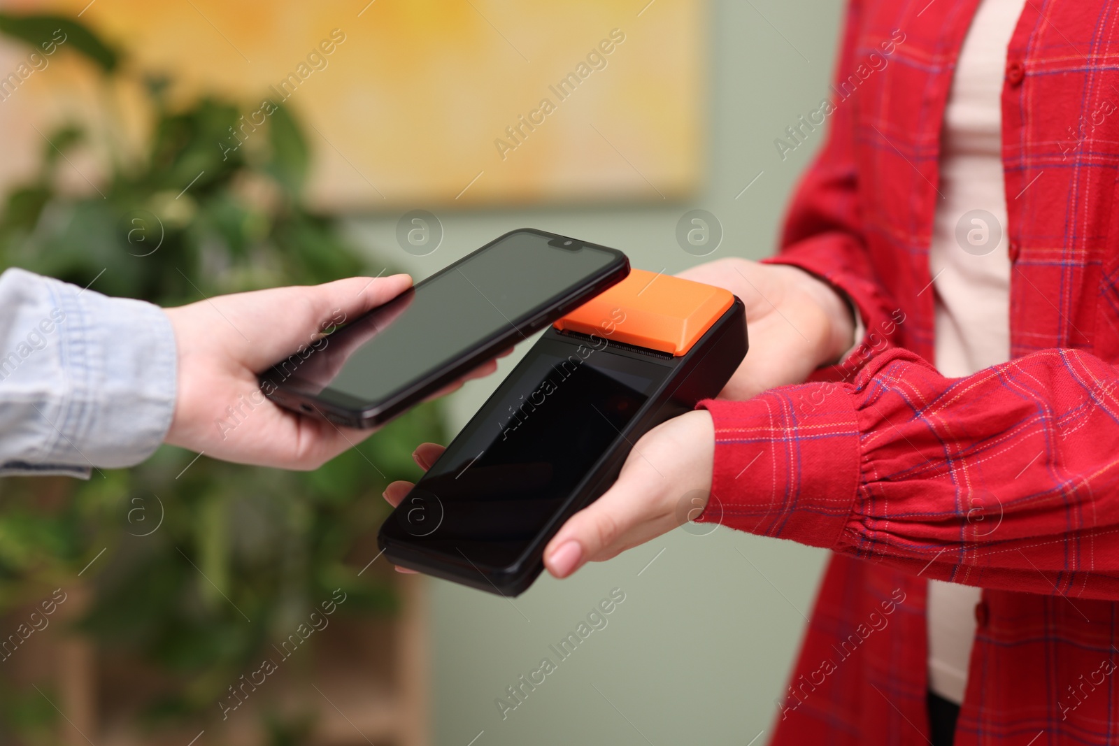 Photo of Woman paying with smartphone via terminal against blurred background, closeup