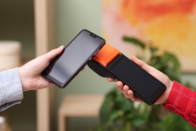 Photo of Woman paying with smartphone via terminal against blurred background, closeup