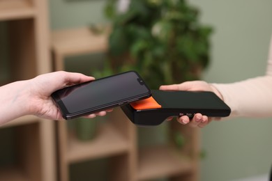 Photo of Woman paying with smartphone via terminal against blurred background, closeup