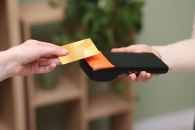 Photo of Woman paying with credit card via terminal against blurred background, closeup