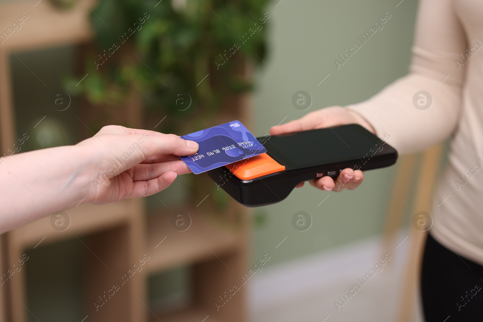 Photo of Woman paying with credit card via terminal against blurred background, closeup