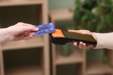 Photo of Woman paying with credit card via terminal against blurred background, closeup