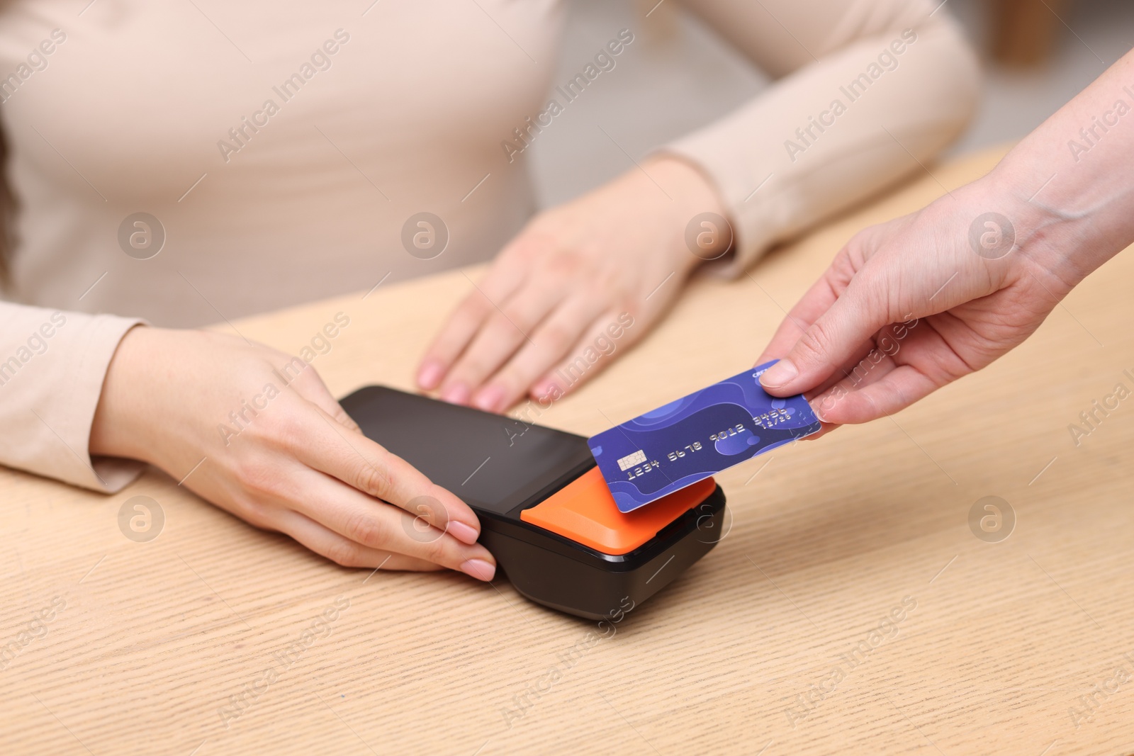 Photo of Woman paying with credit card via terminal at wooden counter indoors, closeup