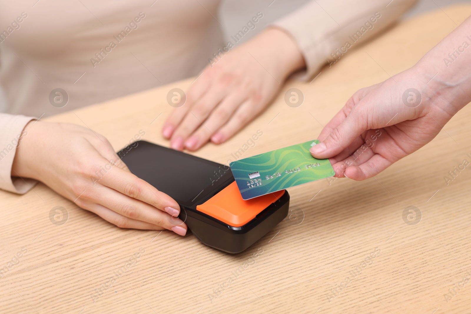 Photo of Woman paying with credit card via terminal at wooden counter indoors, closeup