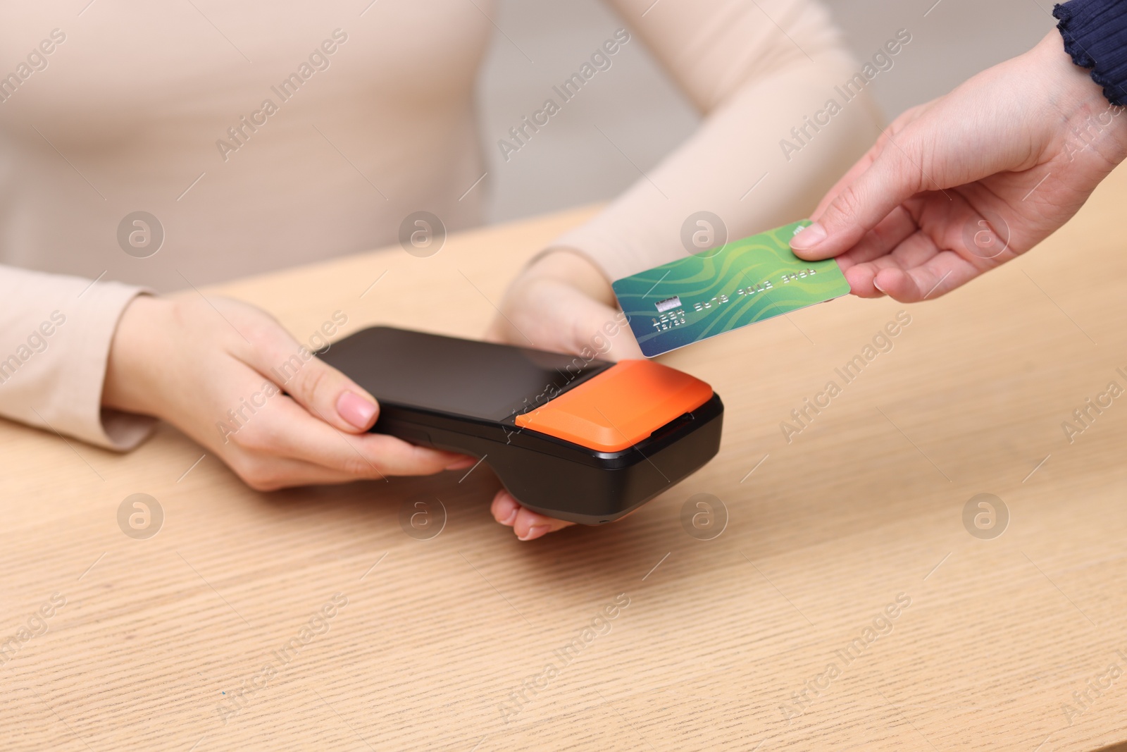 Photo of Woman paying with credit card via terminal at wooden counter indoors, closeup