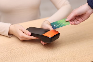 Photo of Woman paying with credit card via terminal at wooden counter indoors, closeup