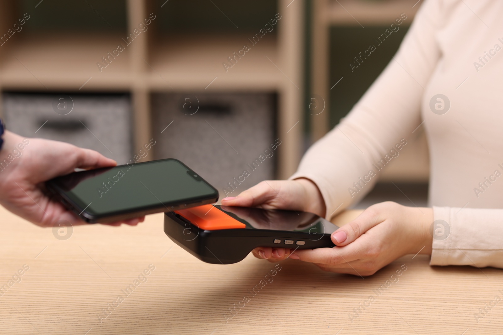 Photo of Woman paying with smartphone via terminal at wooden counter indoors, closeup