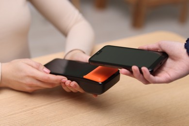 Photo of Woman paying with smartphone via terminal at wooden counter indoors, closeup