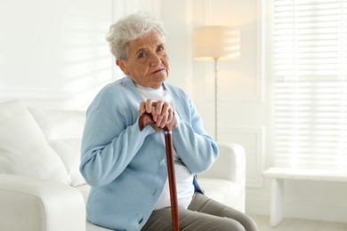 Photo of Lonely senior woman with walking cane sitting on sofa indoors