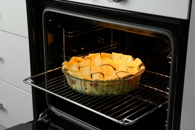 Photo of Baking dish with raw homemade apple pie in oven