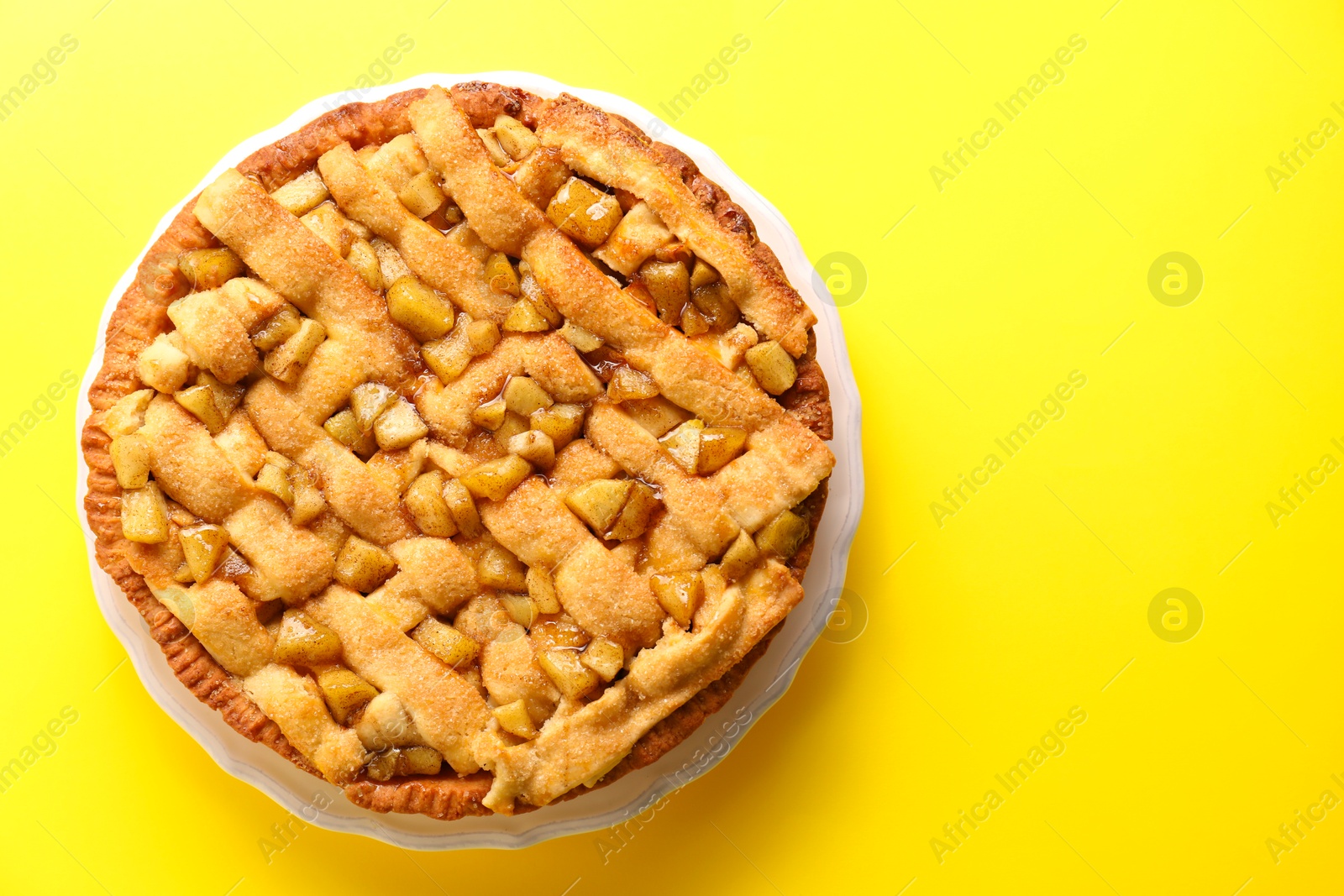 Photo of Tasty homemade apple pie on yellow background, top view. Space for text