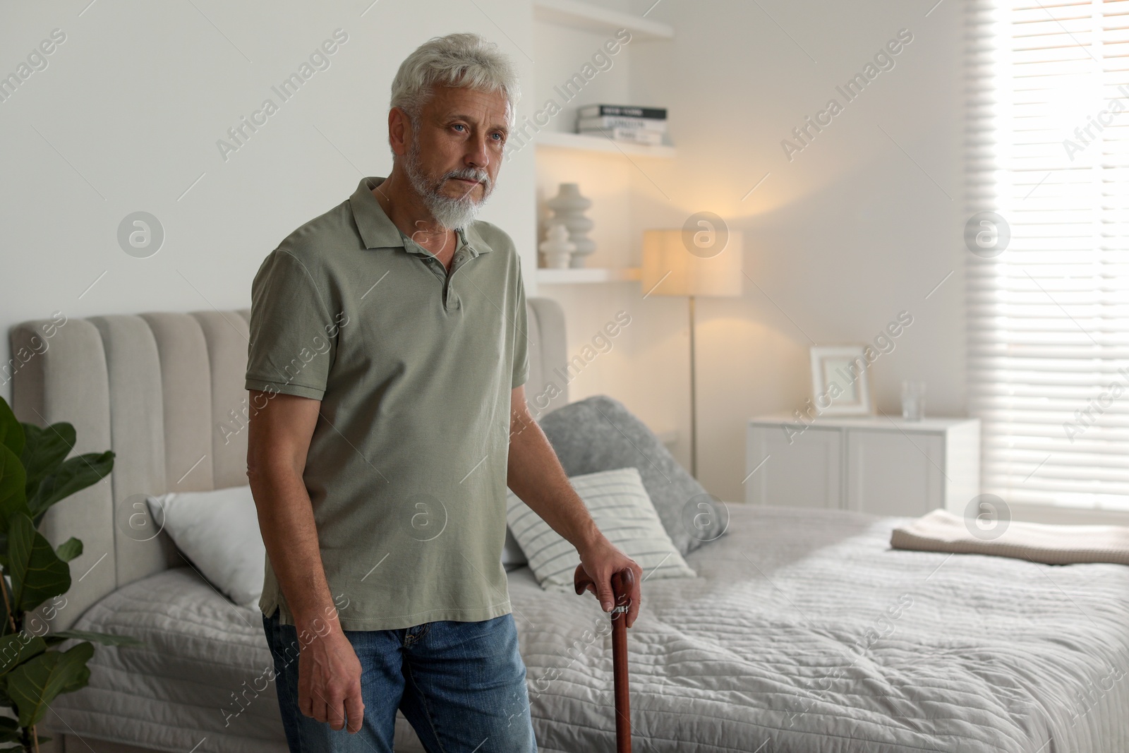 Photo of Lonely senior man with walking cane in bedroom. Space for text