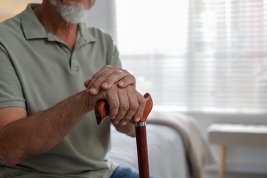 Photo of Lonely senior man with walking cane at home, closeup. Space for text