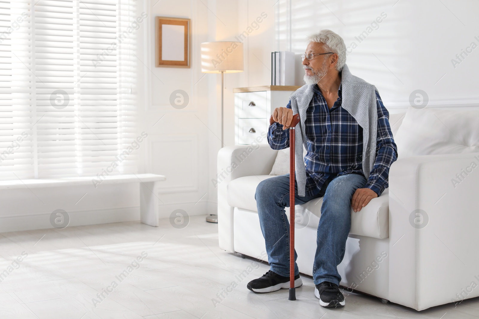 Photo of Lonely senior man with walking cane sitting on sofa at home. Space for text