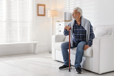 Photo of Lonely senior man with walking cane sitting on sofa at home. Space for text