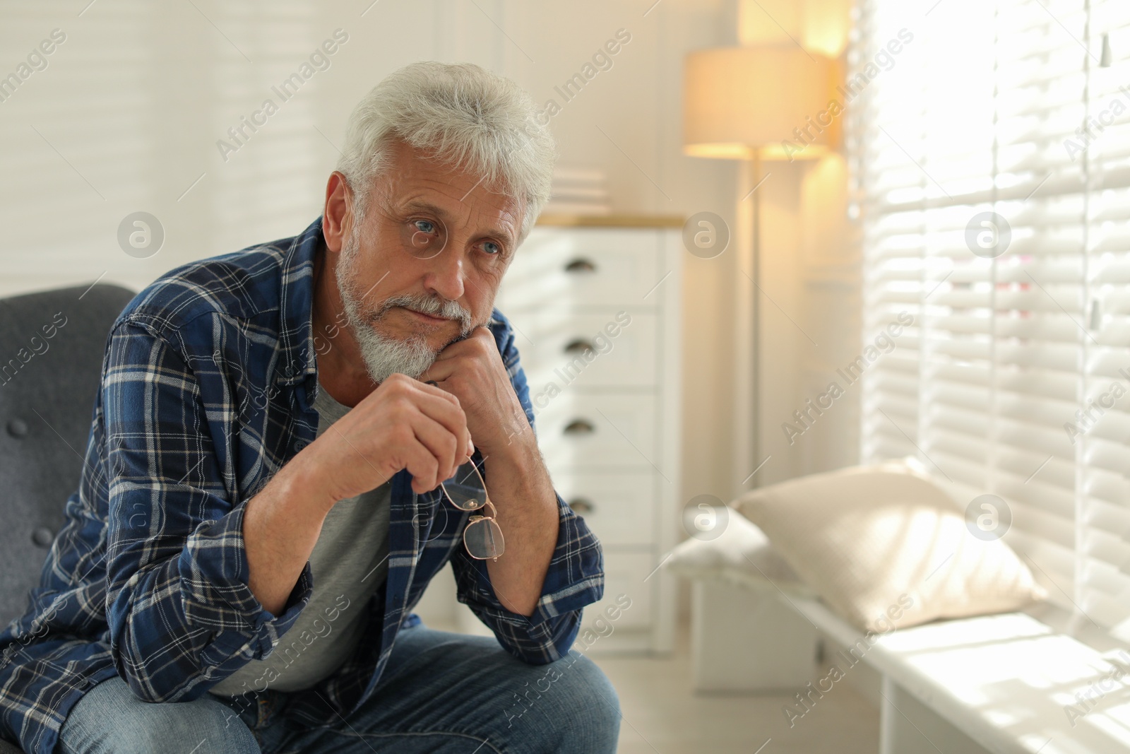 Photo of Lonely senior man sitting in armchair at home. Space for text