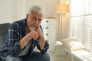 Photo of Lonely senior man sitting in armchair at home. Space for text