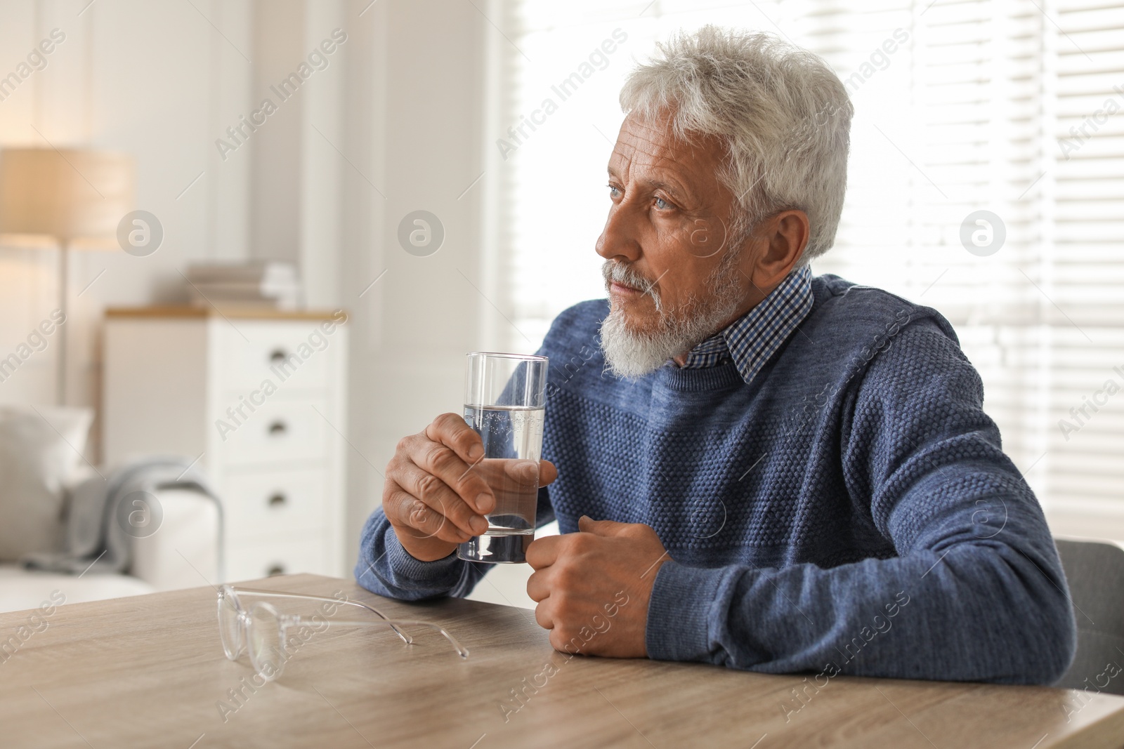 Photo of Lonely senior man with glass of water sitting at table in room