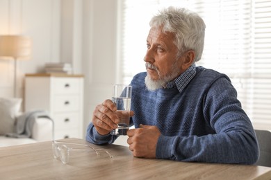 Photo of Lonely senior man with glass of water sitting at table in room