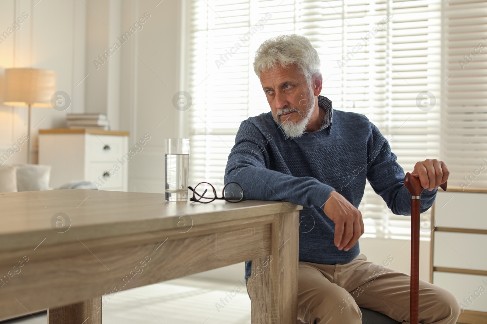 Photo of Lonely senior man with walking cane sitting at table in room