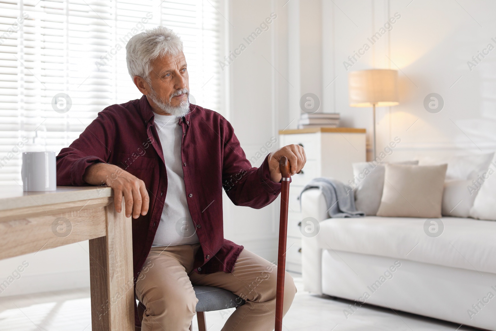 Photo of Lonely senior man with walking cane sitting at table in room