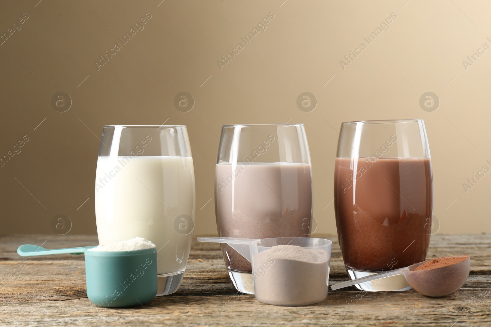 Photo of Different tasty protein cocktails in glasses and powders on wooden table