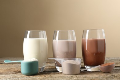 Photo of Different tasty protein cocktails in glasses and powders on wooden table