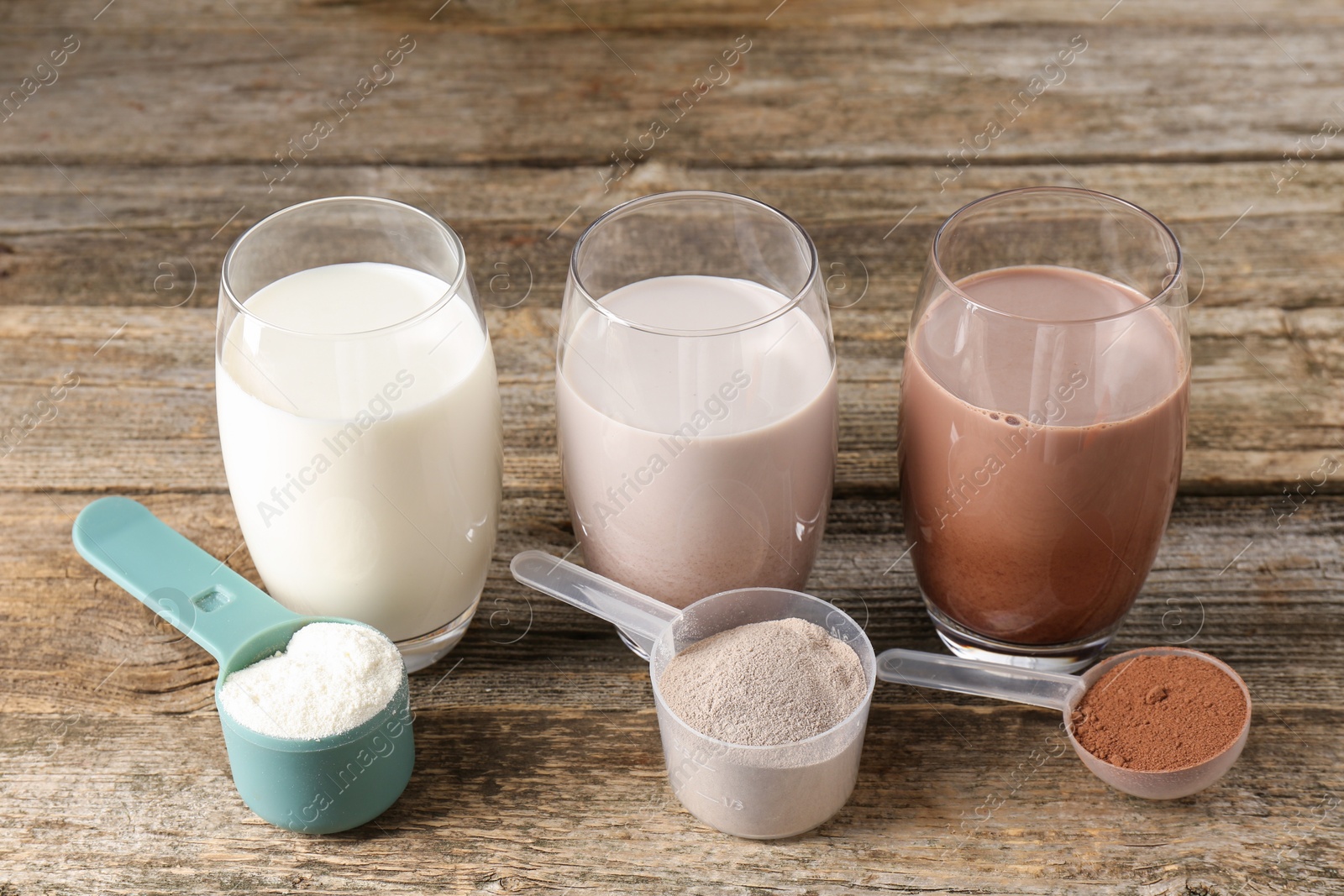 Photo of Different tasty protein cocktails in glasses and powders on wooden table