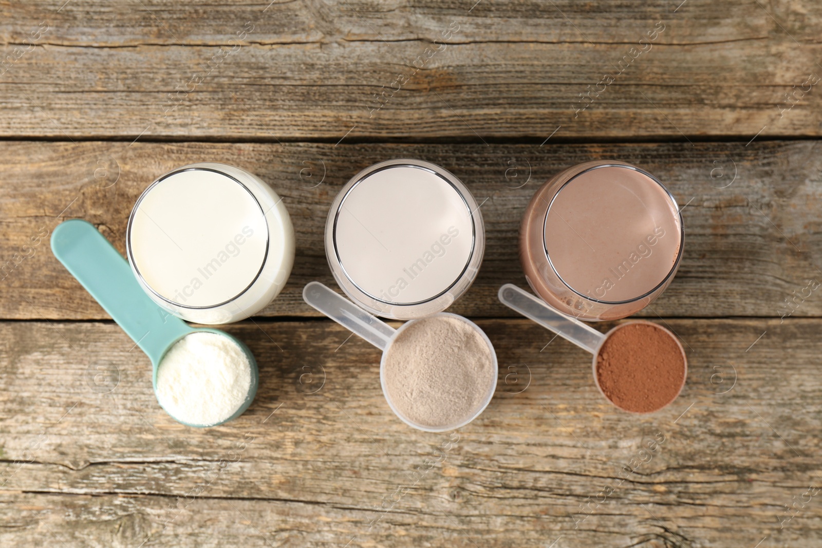 Photo of Different tasty protein cocktails in glasses and powders on wooden table, flat lay