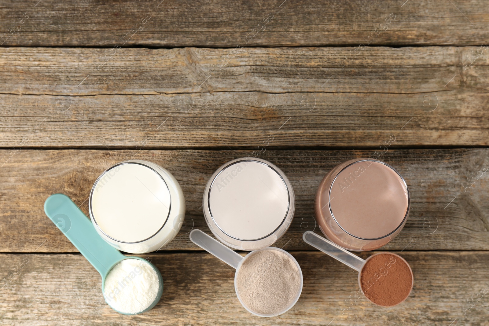 Photo of Different tasty protein cocktails in glasses and powders on wooden table, flat lay. Space for text