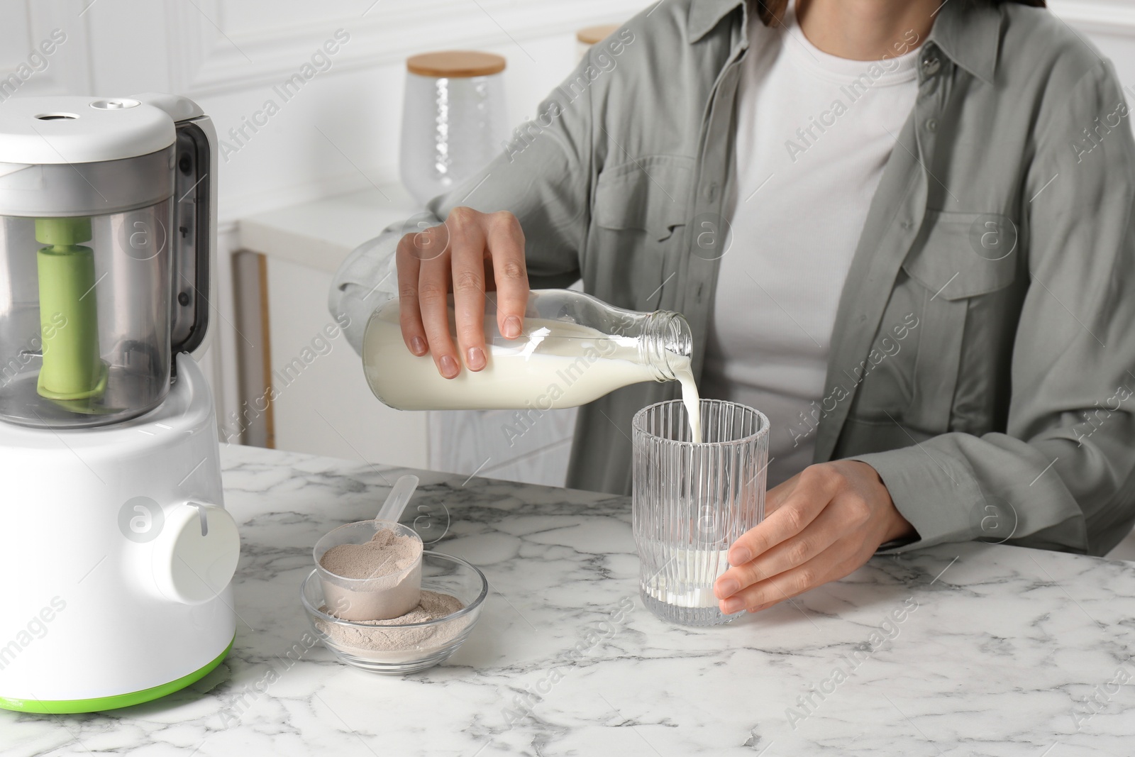 Photo of Making protein cocktail. Woman pouring milk from bottle into glass at white marble table, closeup