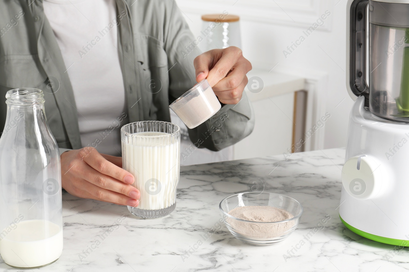 Photo of Making protein cocktail. Woman adding powder into glass with milk at white marble table, closeup