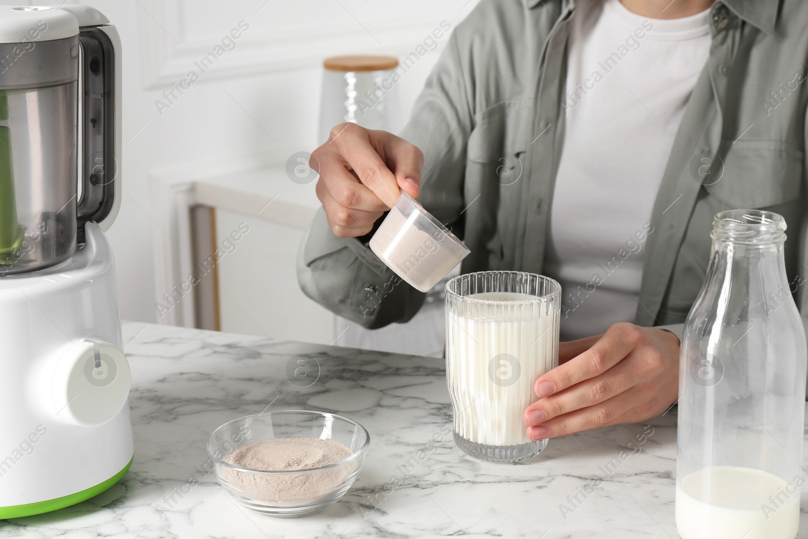 Photo of Making protein cocktail. Woman adding powder into glass with milk at white marble table, closeup