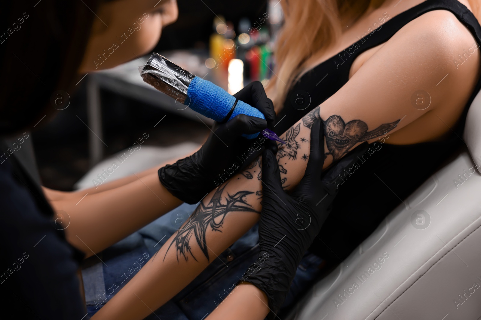 Photo of Professional artist tattooing woman's arm with machine in salon, closeup