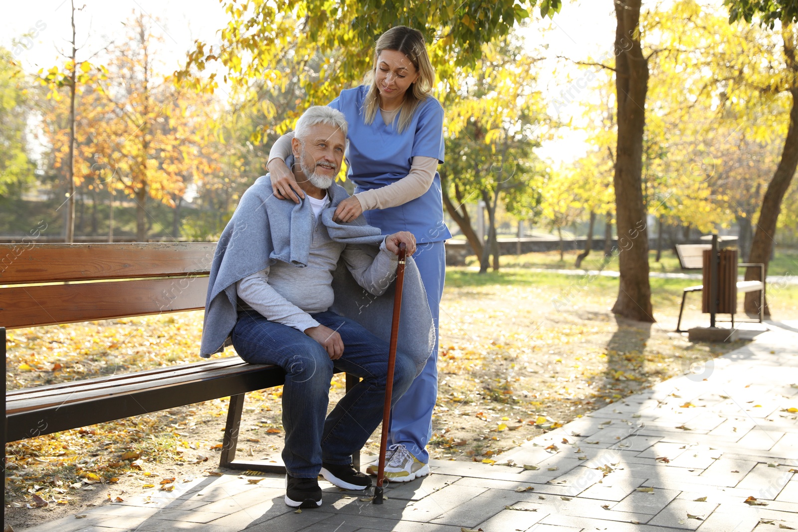 Photo of Caregiver assisting senior man on wooden bench in park, space for text. Home health care service