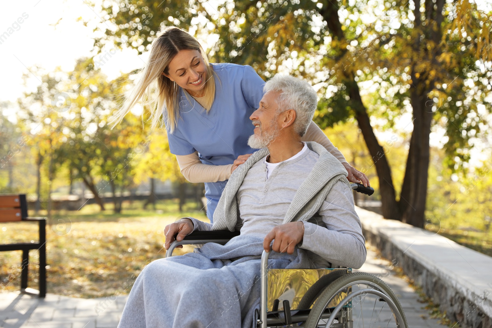 Photo of Caregiver assisting senior man on wheelchair in park. Home health care service