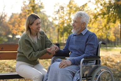 Photo of Caregiver assisting senior man on wheelchair in park. Home health care service