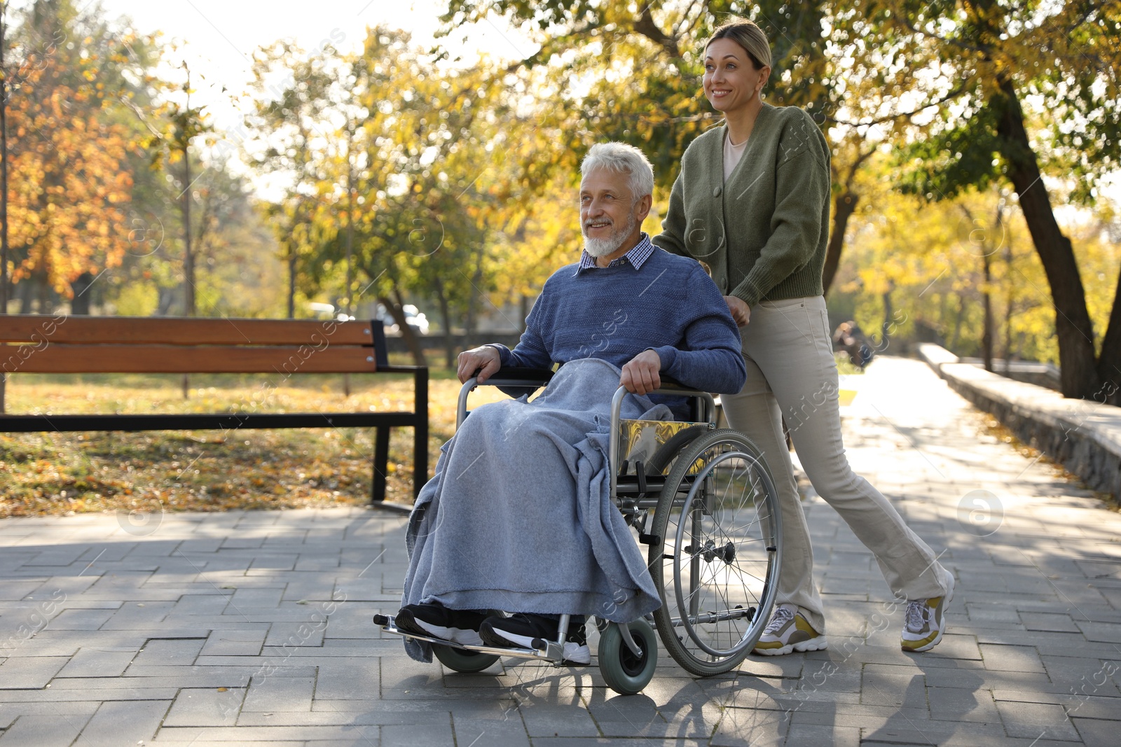 Photo of Caregiver assisting senior man on wheelchair in park, space for text. Home health care service