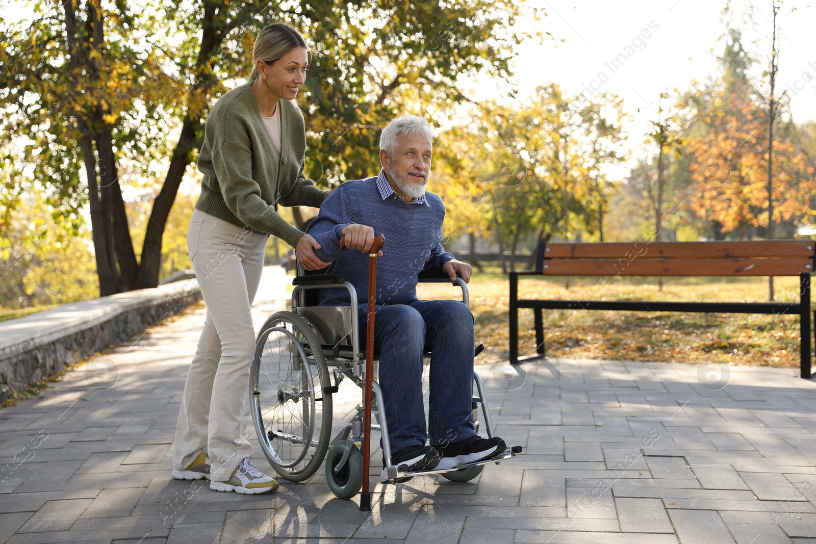 Photo of Caregiver assisting senior man on wheelchair in park, space for text. Home health care service