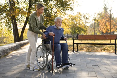 Photo of Caregiver assisting senior man on wheelchair in park, space for text. Home health care service