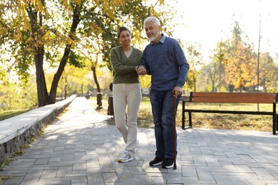 Photo of Caregiver assisting senior man in park. Home health care service