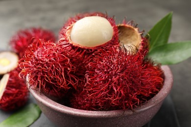 Photo of Delicious ripe rambutans and green leaves on table, closeup