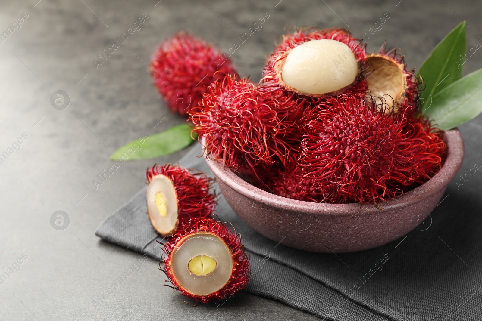 Photo of Delicious ripe rambutans and green leaves on grey table, closeup. Space for text