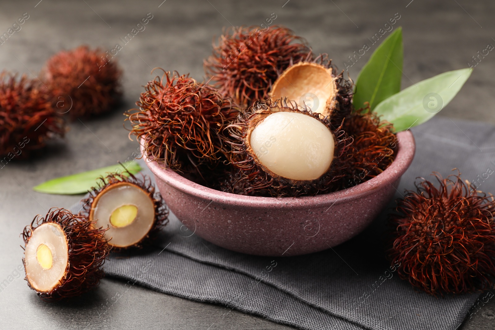 Photo of Delicious ripe rambutans and green leaves on grey table, closeup